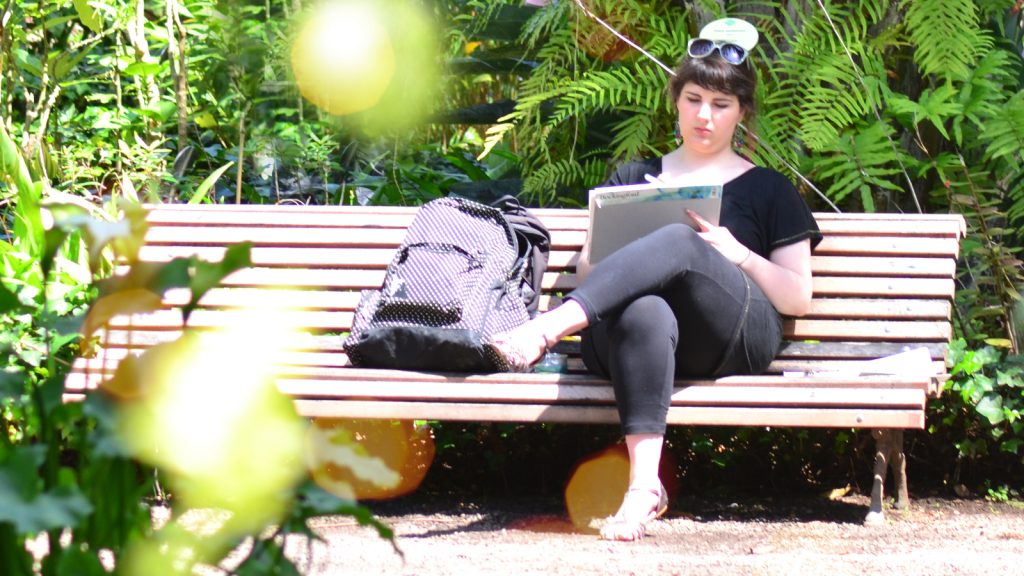 A photo of Charlotte Thomson Morley painting in a garden while sitting on a bench