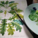 a photograph of a green nature goddess made up of leaves painted in watercolour next to a palette and paintbrush