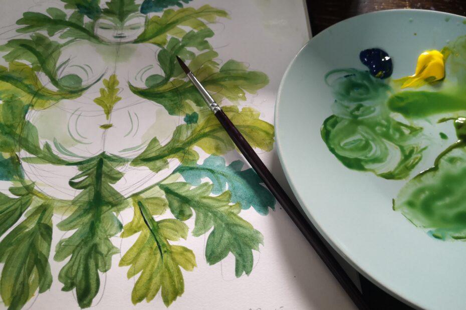 a photograph of a green nature goddess made up of leaves painted in watercolour next to a palette and paintbrush